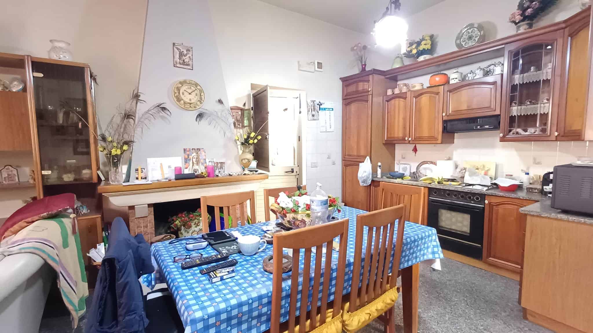 Piatto da pranzo con tovaglia a scacchi blu in cucina tradizionale con mobili in legno, stoviglie e decorazioni floreali, ambiente accogliente e luminoso.