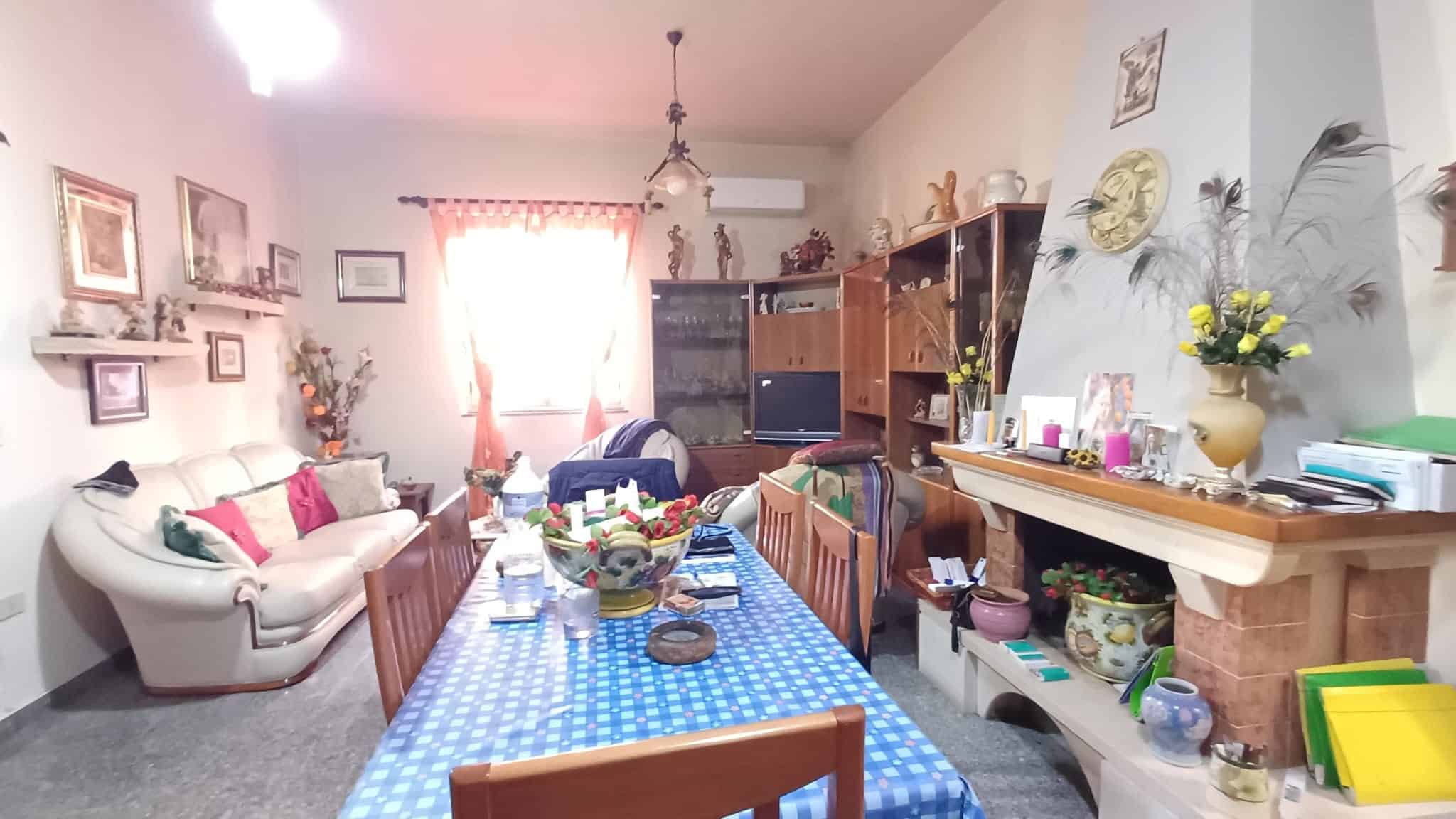 Ampia sala da pranzo e soggiorno con divani, tavolo centrale e decorazioni floreali, ambiente accogliente e luminoso, ideale per momenti di convivialità e relax.