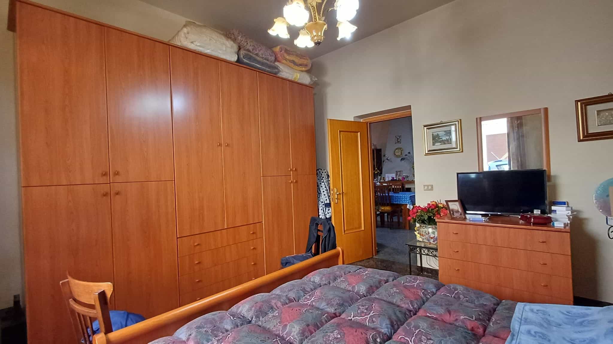 Armadio a muro in legno e camera da letto con letto matrimoniale, televisore e decorazioni classiche, ambiente accogliente e ben organizzato.