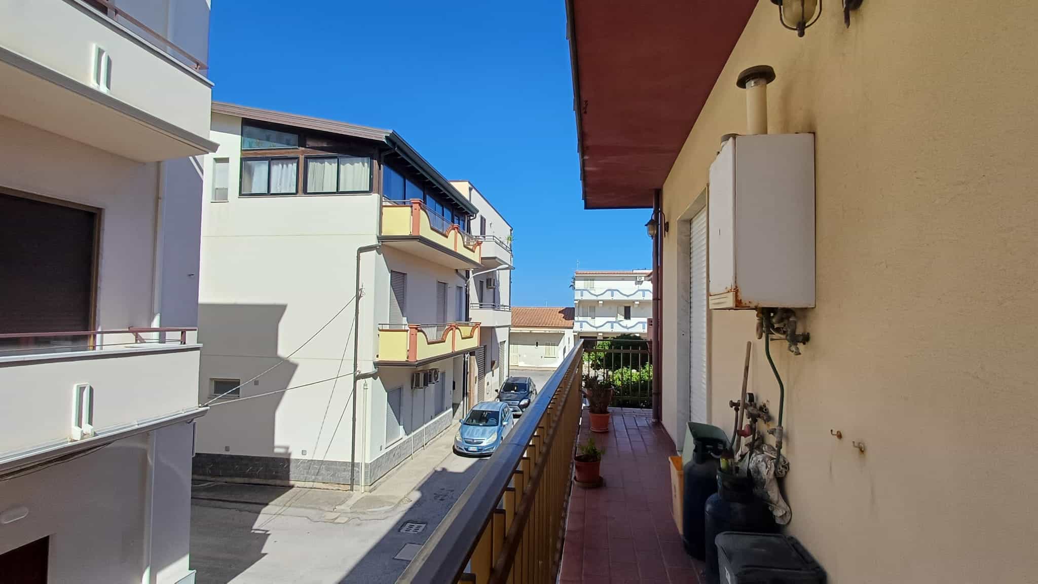 Ampio balcone con vista su strada urbana, con piante e arredi esterni, in un complesso residenziale moderno, ideale per relax e socializzazione all'aperto.