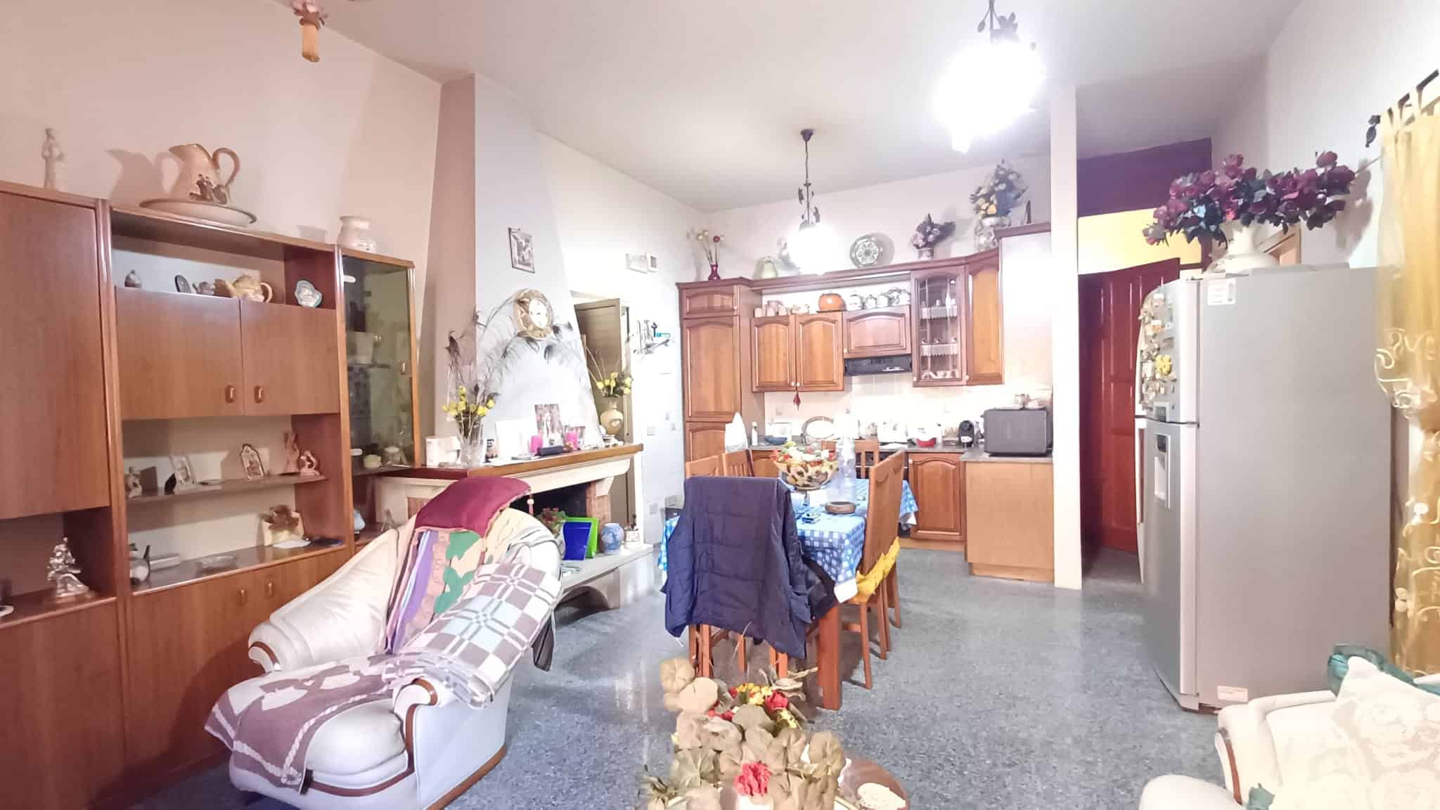 Interno di una cucina e zona pranzo con arredi in legno, divano e decorazioni floreali, ambiente accogliente e luminoso.