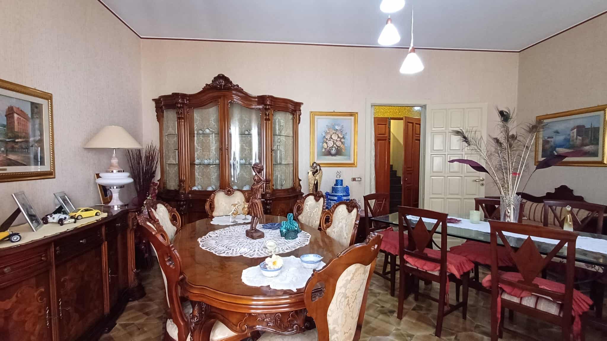 Antico tavolo da pranzo in legno con sedie imbottite, in una sala da pranzo tradizionale con mobili d'epoca, decorazioni eleganti e quadri alle pareti, ambiente accogliente e raffinato.