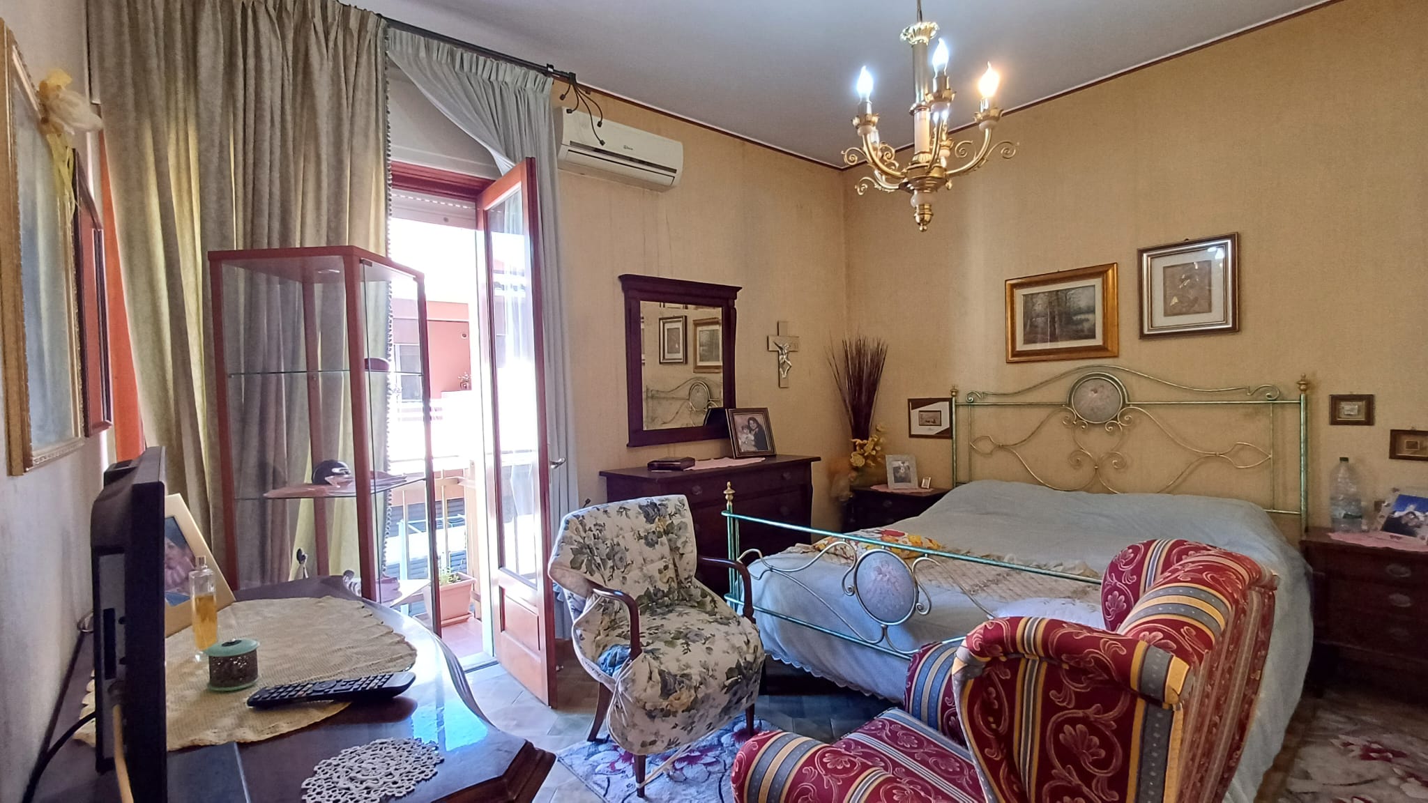 Ampia camera da letto con letto matrimoniale, sedie e mobili classici, balcone con vista luminosa, decorazioni eleganti e atmosfera accogliente, ideale per soggiorni confortevoli e rilassanti.