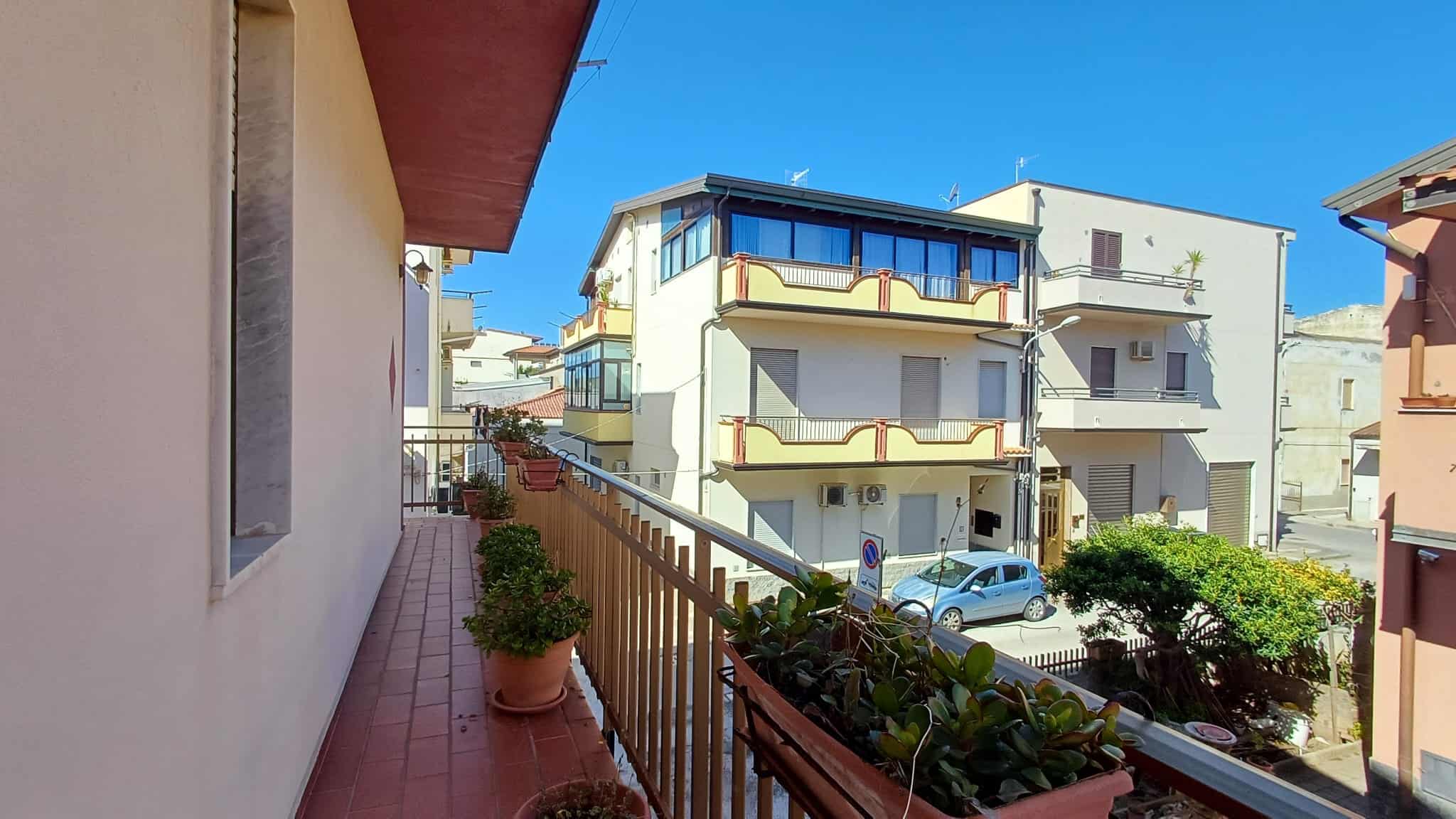 Balcone di un appartamento con piante ornamentali e vista su strada urbana, in un quartiere residenziale soleggiato.