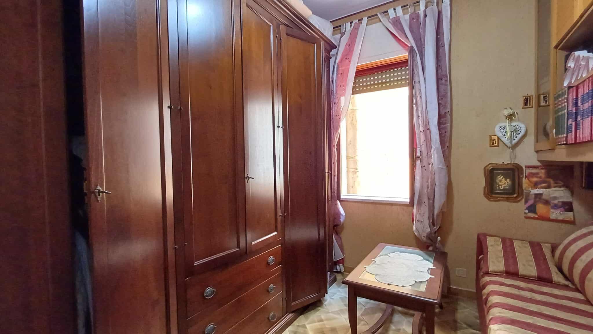 Armadio in legno massiccio in una camera da letto con finestra e tende rosa, stile classico e caldo.