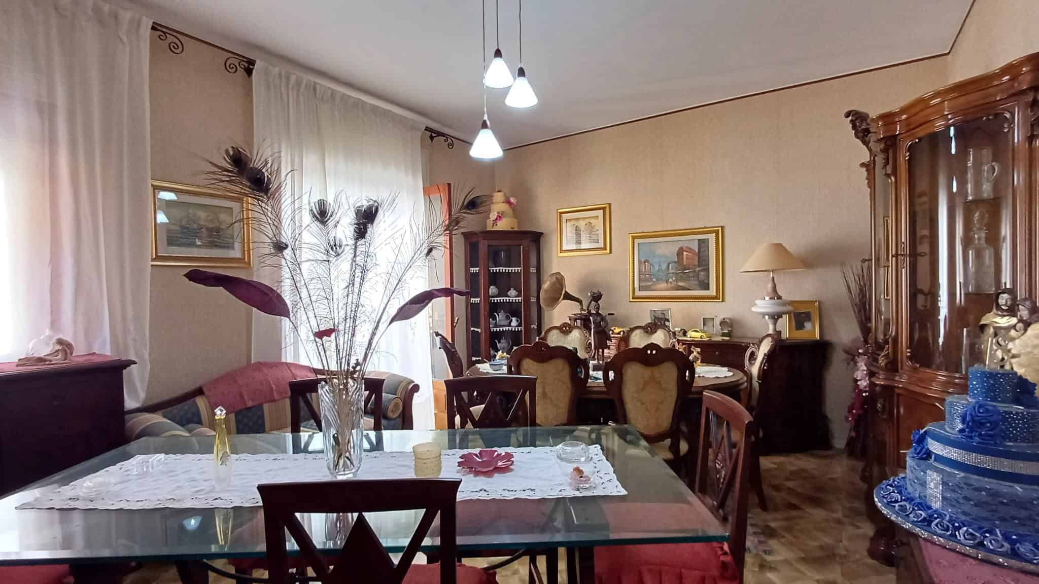 Elegante sala da pranzo con mobili classici, tavolo in vetro, decorazioni floreali e illuminazione soffusa, ideale per convivialità e momenti di relax in un ambiente raffinato.