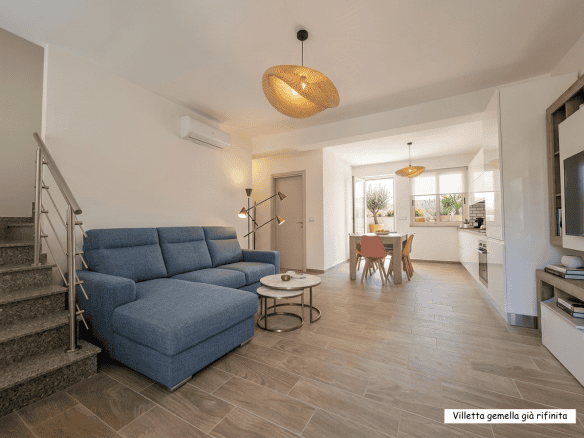 Ampia zona living moderna con divano blu, illuminazione calda e cucina a vista, ideale per soggiorni confortevoli e conviviali in un appartamento di design.