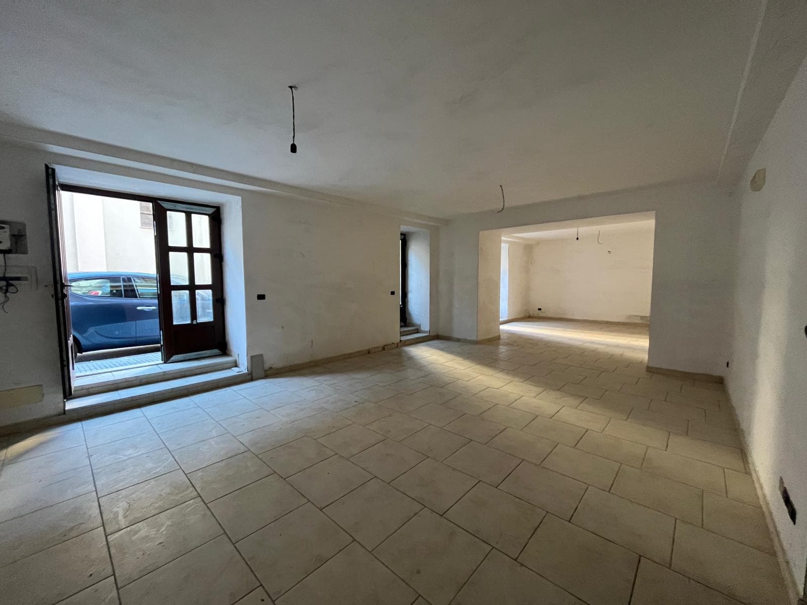 Ampio spazio interno di un appartamento in fase di ristrutturazione, con pareti bianche e pavimento in piastrelle beige, pronto per essere personalizzato.