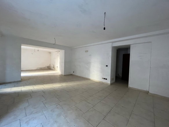 Ampio soggiorno in fase di ristrutturazione con pareti bianche e pavimento in piastrelle beige, pronto per essere personalizzato e arredato. Ideale per creare un ambiente luminoso e accogliente.