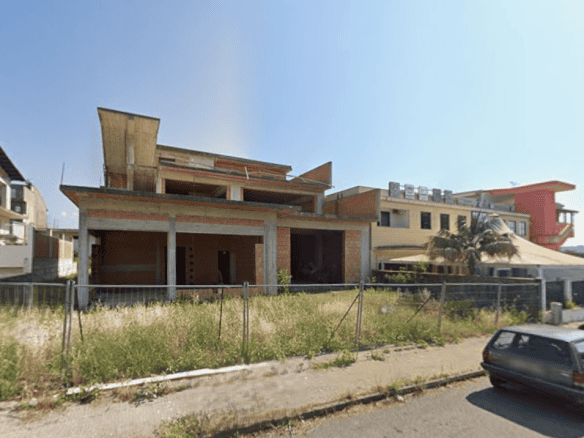 Ampia casa in costruzione con struttura in cemento e mattoni, situata in un'area residenziale soleggiata e tranquilla, pronta per essere completata e personalizzata.