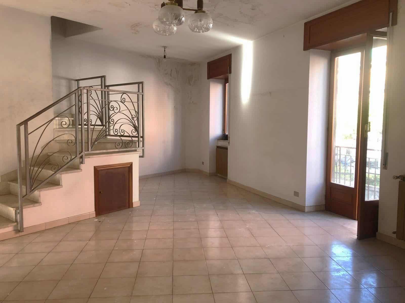 Interno di un soggiorno spazioso con grandi finestre, balcone e scale in metallo decorativo, ideale per ambienti moderni e luminosi.