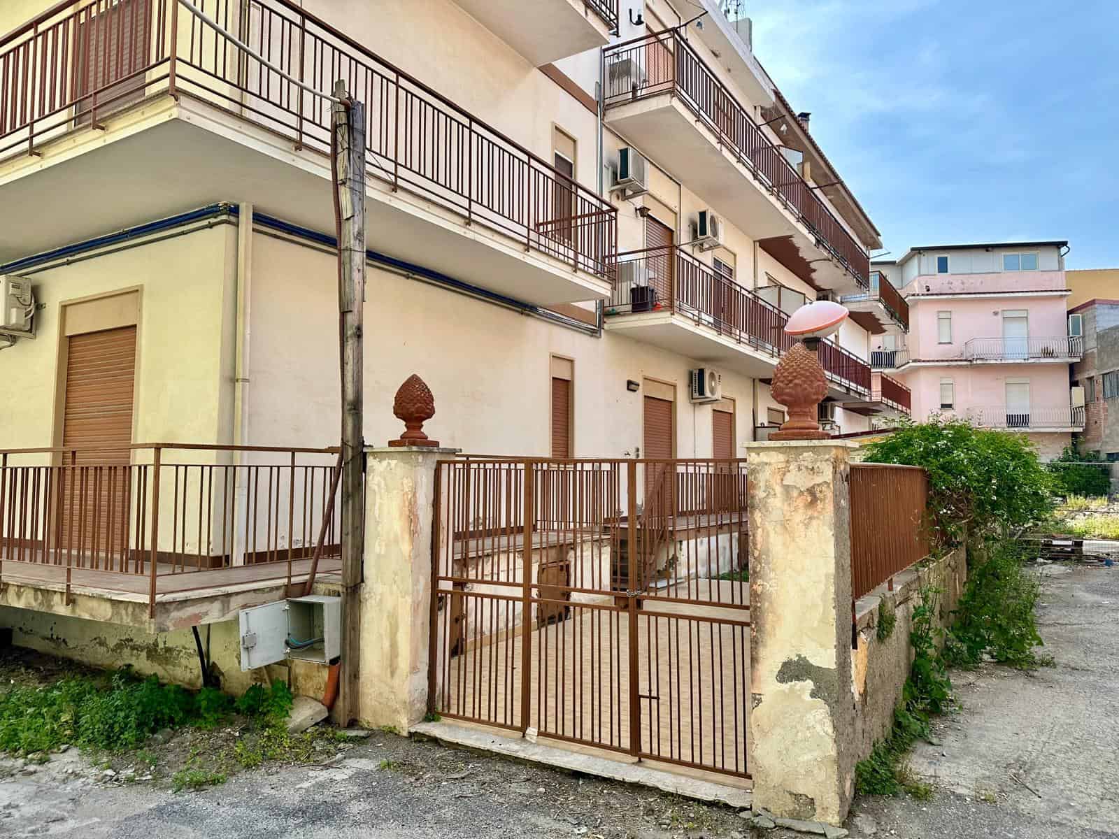 Edificio residenziale con balconi e recinzione in ferro battuto, in un'area urbana. Facciata con balconi e accesso tramite cancello in ferro, in un contesto di quartiere residenziale.