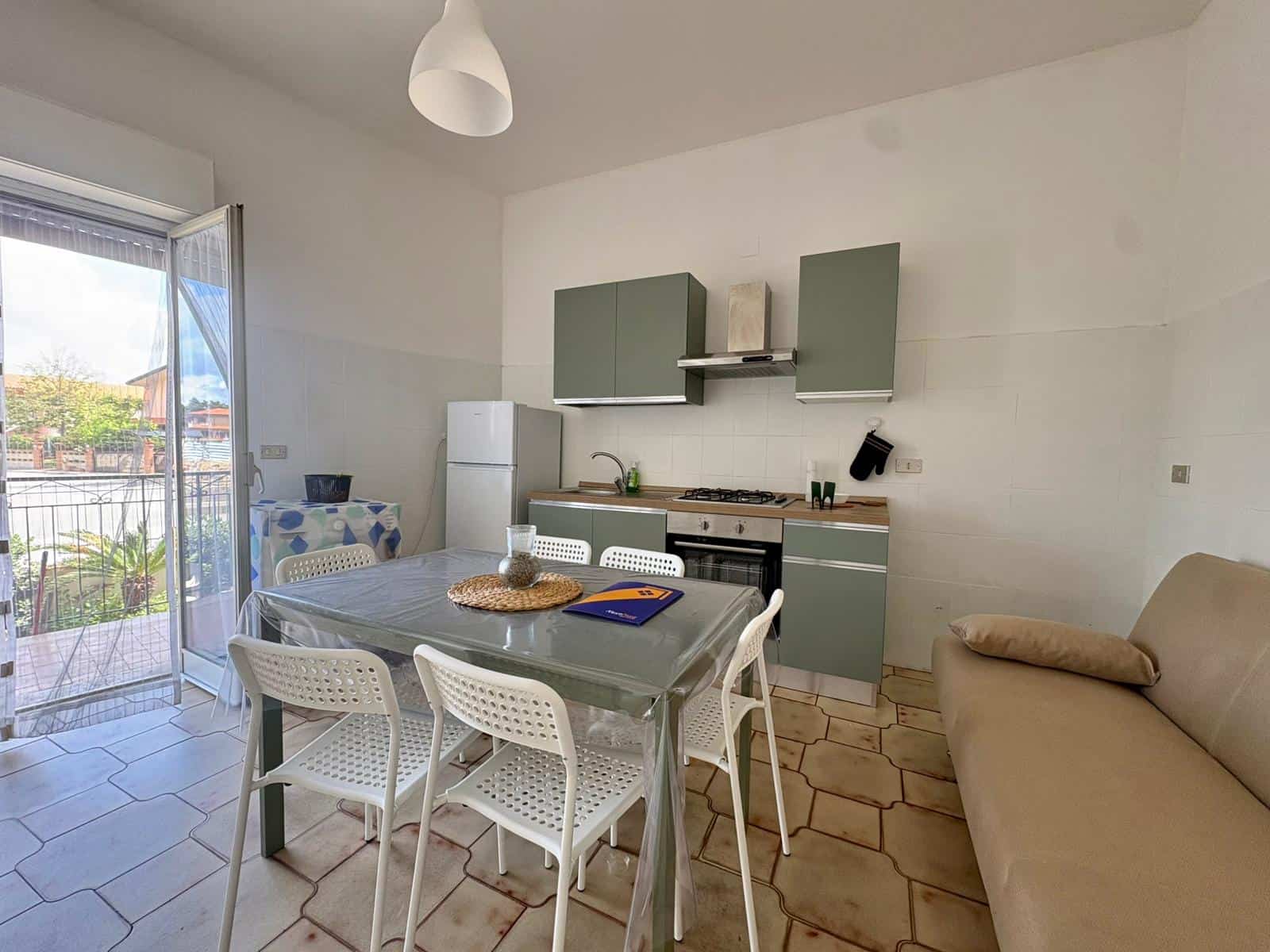 Casa moderna con cucina e zona pranzo luminosa. Interno di una casa moderna con cucina compatta e zona pranzo luminosa, con mobili minimalisti, tavolo con sedie bianche, e accesso a un balcone con vista all'aperto.