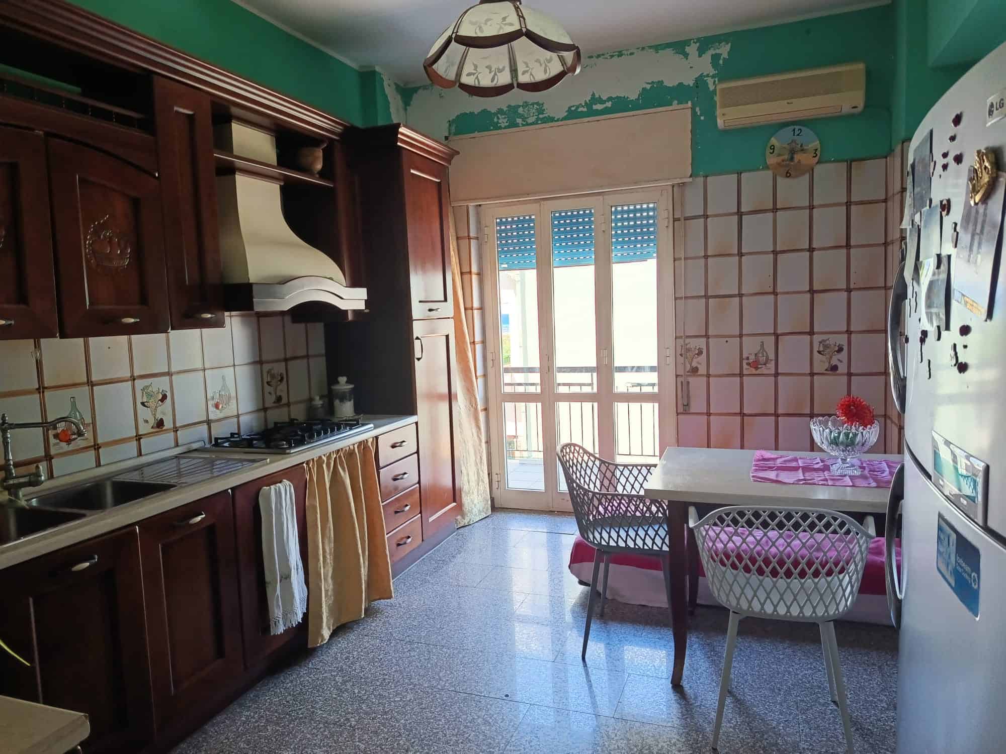Cucina spaziosa con balcone, mobili in legno scuro, piano cottura a gas e frigorifero, ideale per famiglie e conviviale.