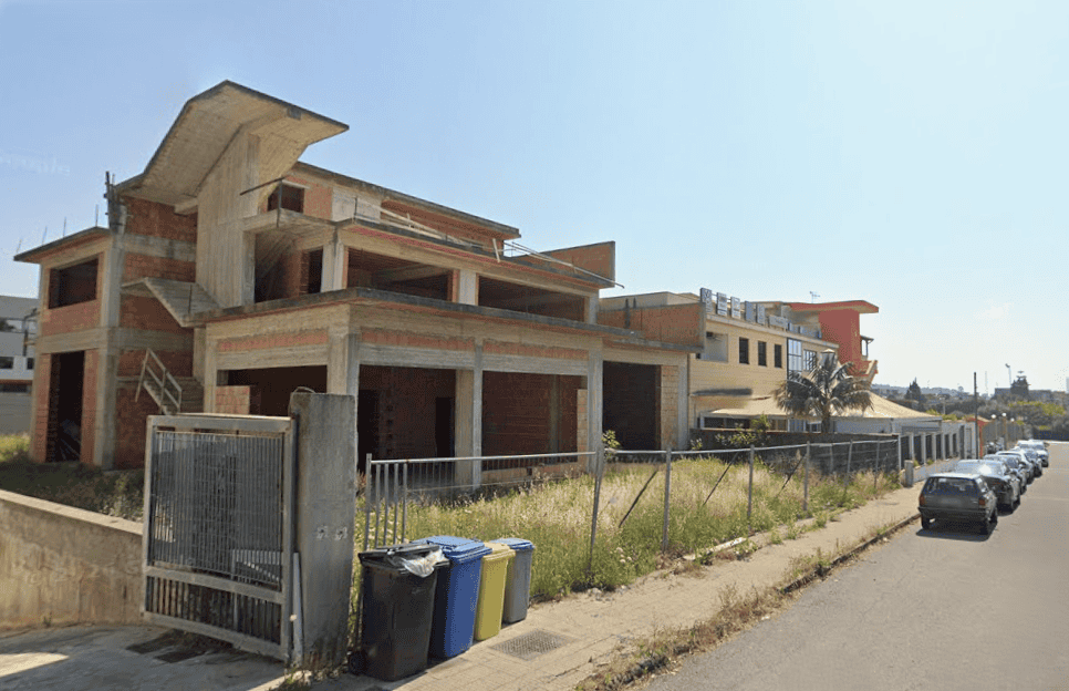 L'immagine mostra un edificio in costruzione in un'area residenziale, con strutture in cemento e mattoni, pronto per essere completato.