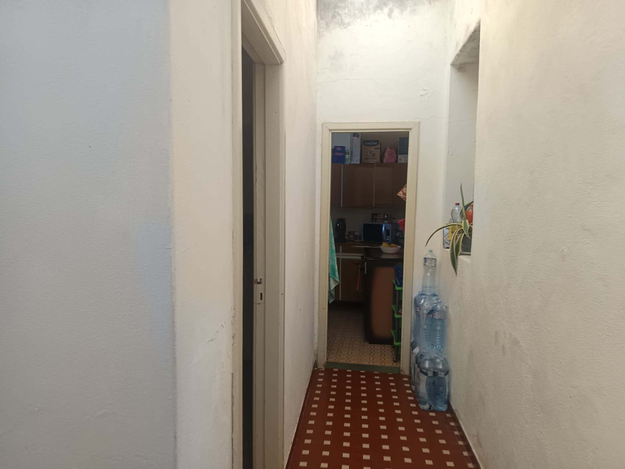 Corridoio interno con spazio di servizio, armadietti e bottiglie d'acqua, in un ambiente domestico ordinato e funzionale.