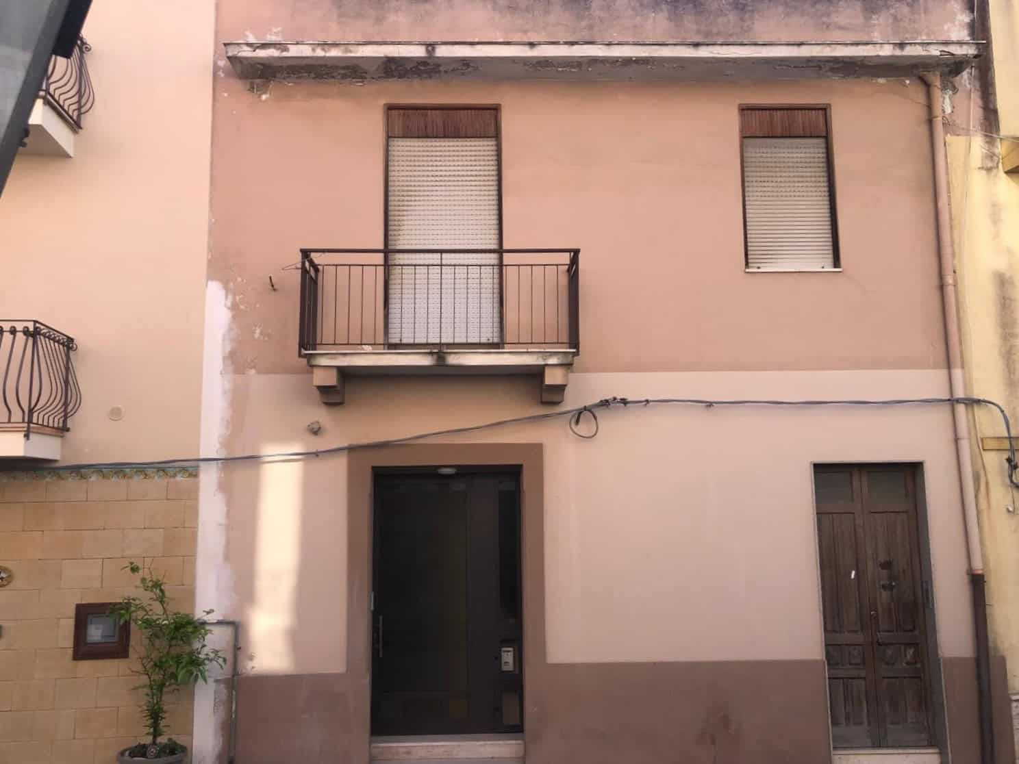 Porta d'ingresso moderna con balcone e finestre in una facciata di edificio residenziale, pareti in tonalità neutre e dettagli architettonici semplici, in un contesto urbano.