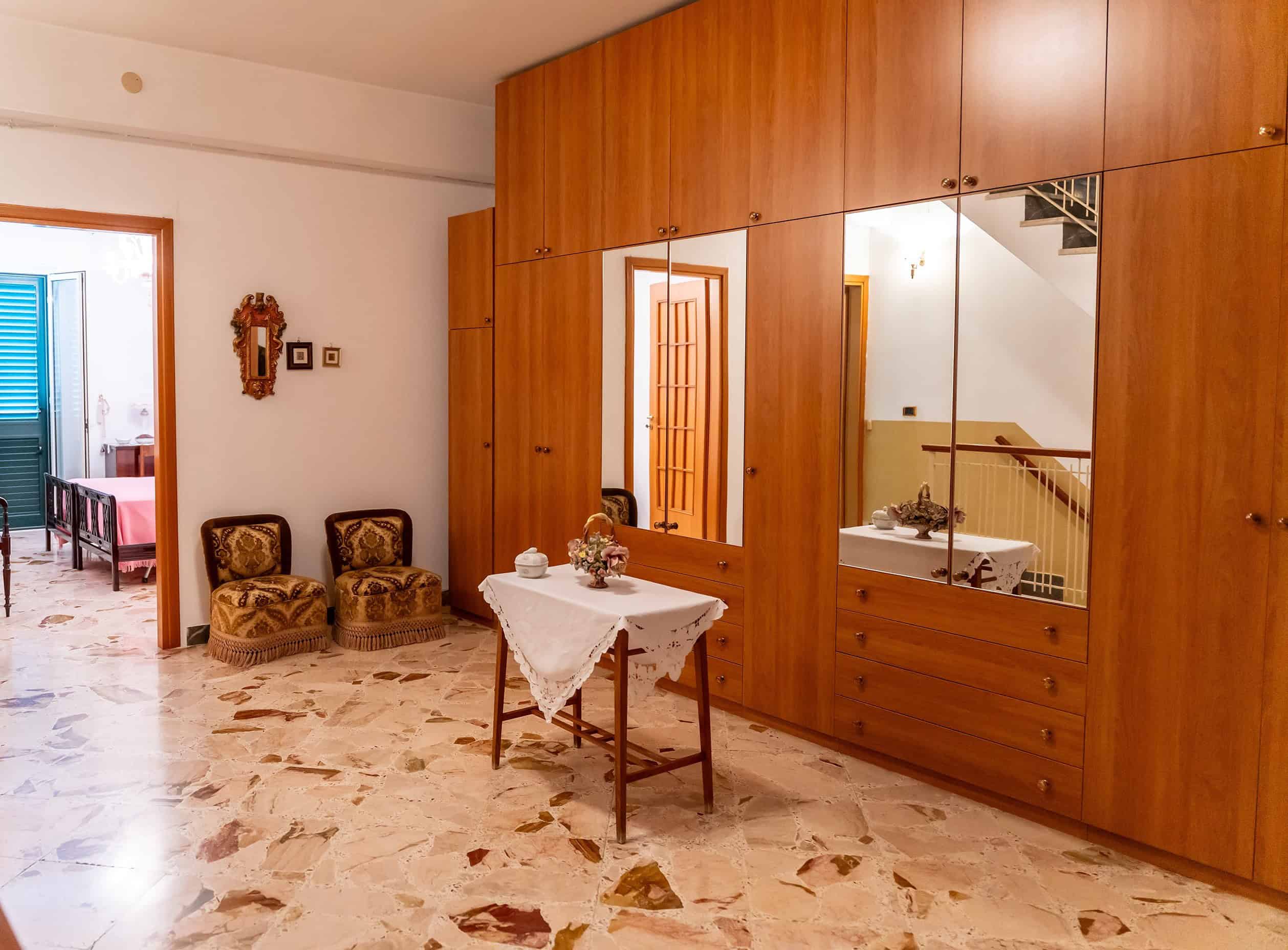 Interno di un appartamento con mobili in legno, tavolo decorato e pareti con specchi, ambiente luminoso e accogliente, ideale per affitti turistici o residenziali in Italia.