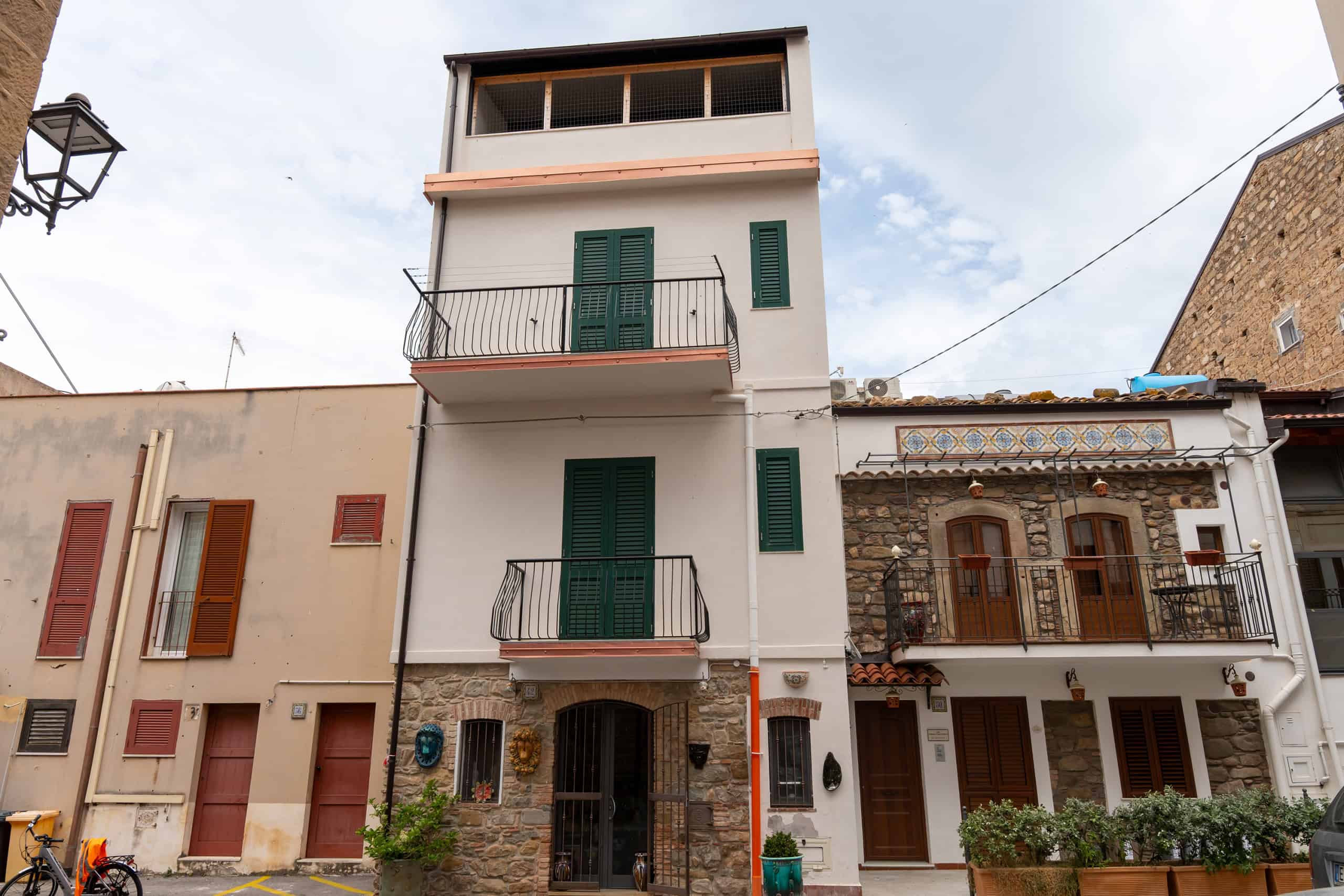 Edificio residenziale moderno con balconi e finestre verdi, situato in zona urbana di Napoli, Italia, con cielo nuvoloso sullo sfondo.