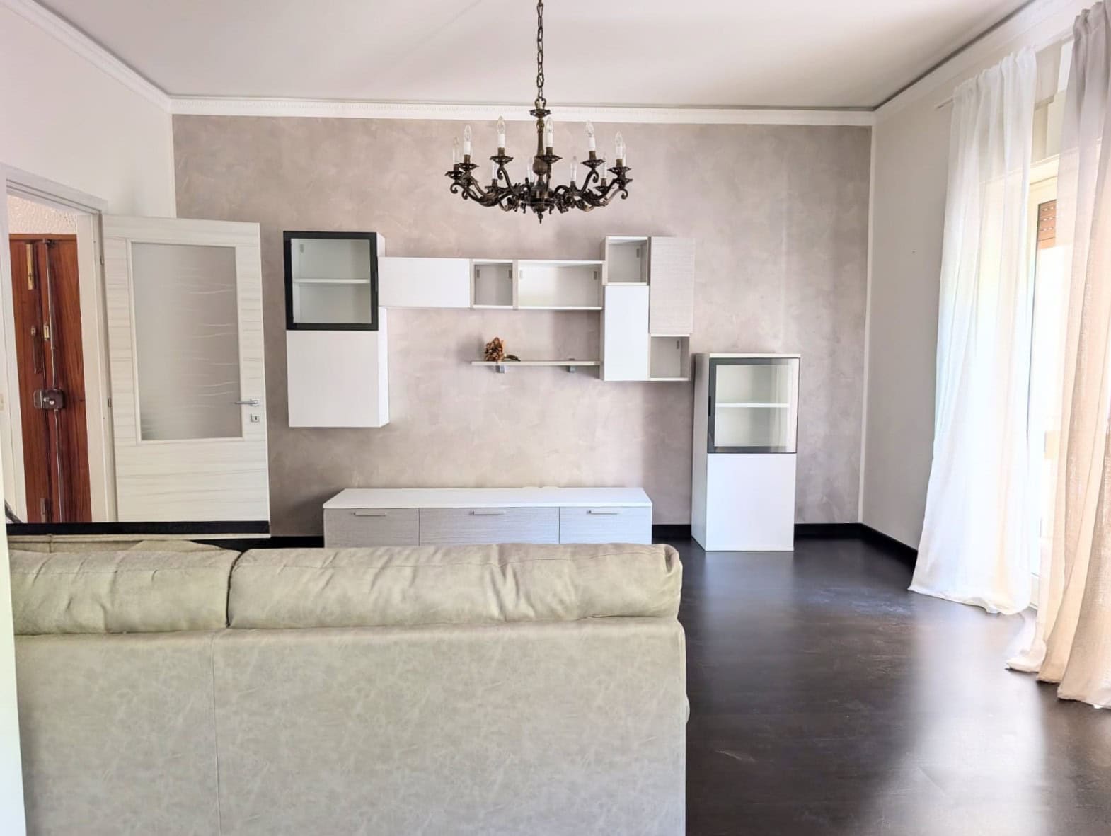 Aria moderna e luminosa con pareti neutre, mobili minimalisti e grande finestra con tende leggere, ideale per un soggiorno elegante e accogliente.