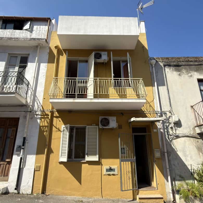 Edificio residenziale con balcone e aria condizionata, facciata gialla e dettagli in bianco, in zona urbana soleggiata.