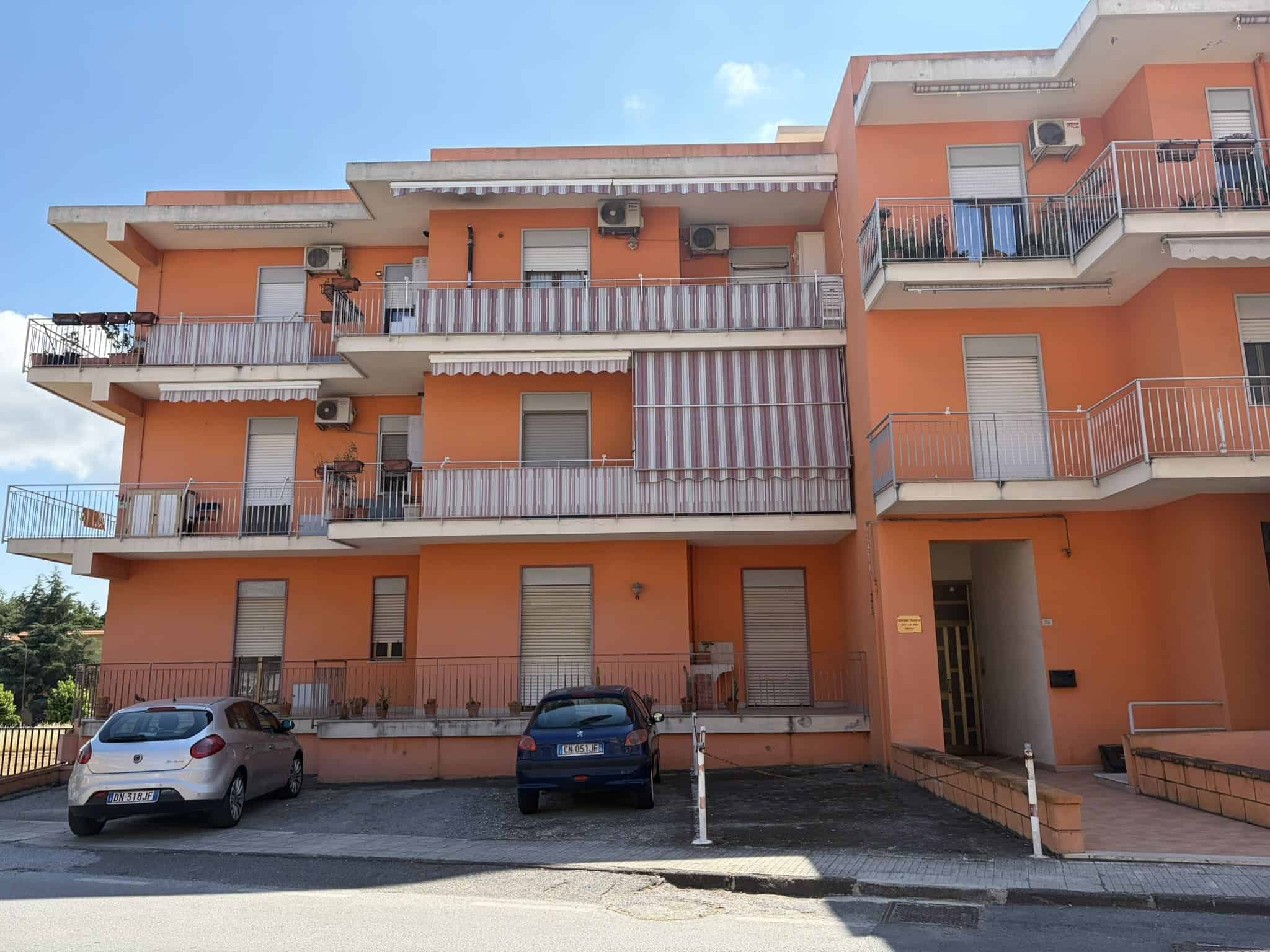 1 Edificio residenziale a tre piani con balconi e aria condizionata, in zona urbana, con parcheggio frontale e accesso pedonale.