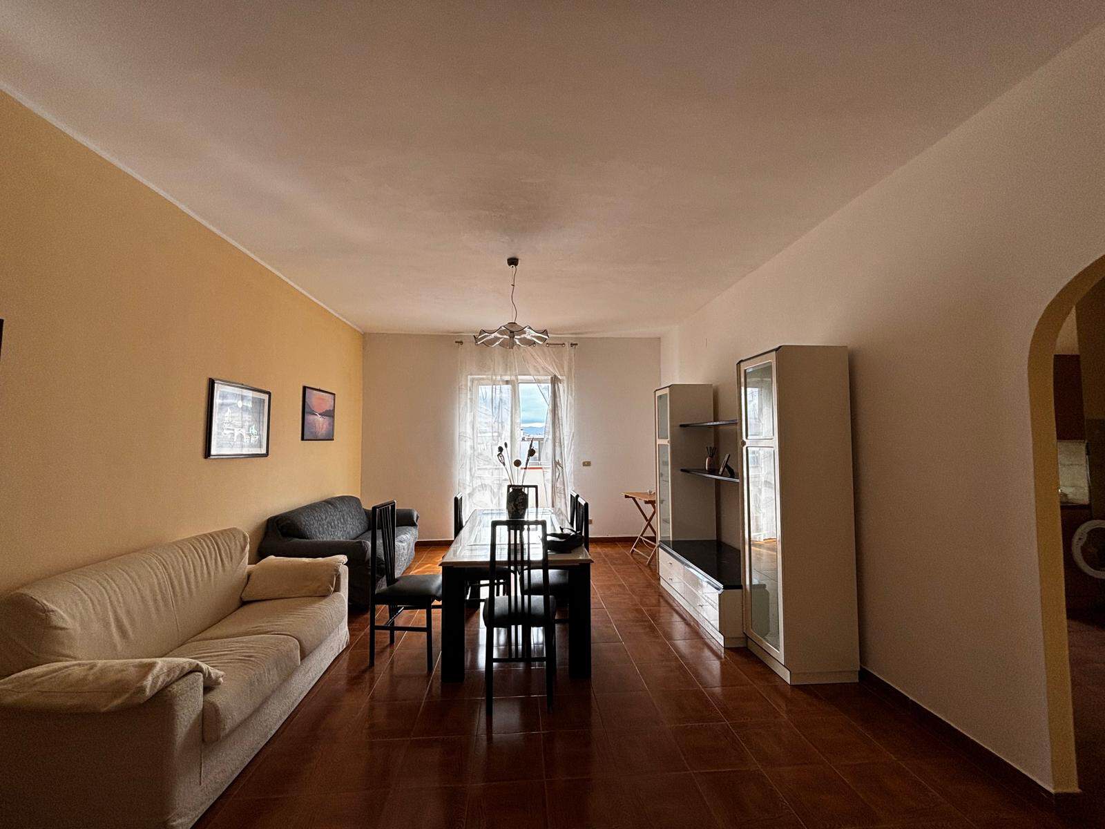 Ampia zona living con divani e tavolo da pranzo, illuminata da luce naturale, in un appartamento moderno in Italia, ideale per famiglie e coppie, con arredi funzionali e atmosfera accogliente.