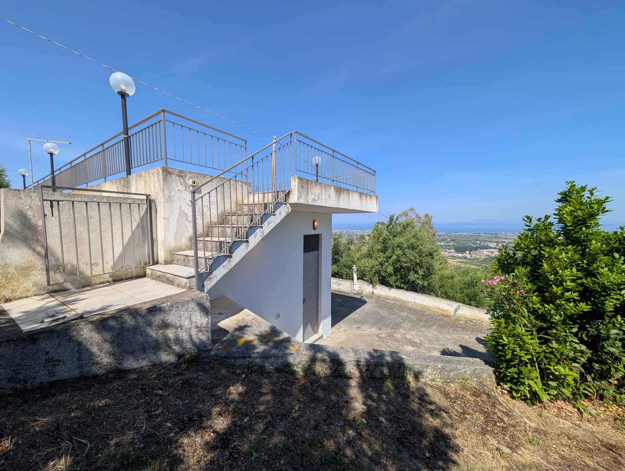Balcone panoramico con ringhiera in metallo, vista aperta su paesaggi verdi e cielo azzurro, situato su una terrazza di una casa in collina, ideale per relax e godersi il panorama naturale.
