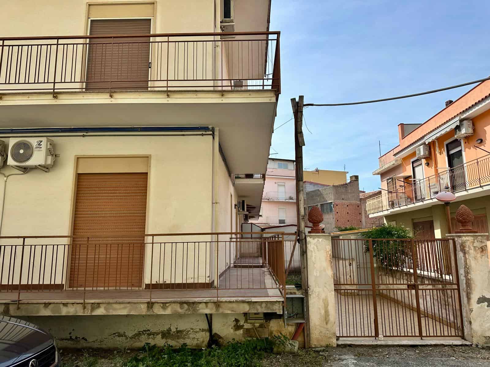 Edificio residenziale con balconi e cancello in ferro, vista urbana in zona tranquilla, cielo sereno, dettagli di facciata e infrastrutture locali.
