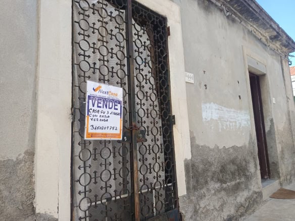 Cancello in ferro battuto con cartello di vendita, situato su una parete esterna di una casa in condizioni di deterioramento, in un contesto urbano italiano.