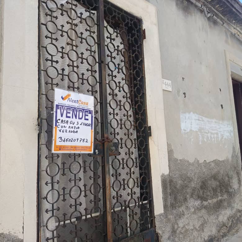 Cancello in ferro battuto con cartello di vendita, situato su una parete esterna di una casa in condizioni di deterioramento, in un contesto urbano italiano.