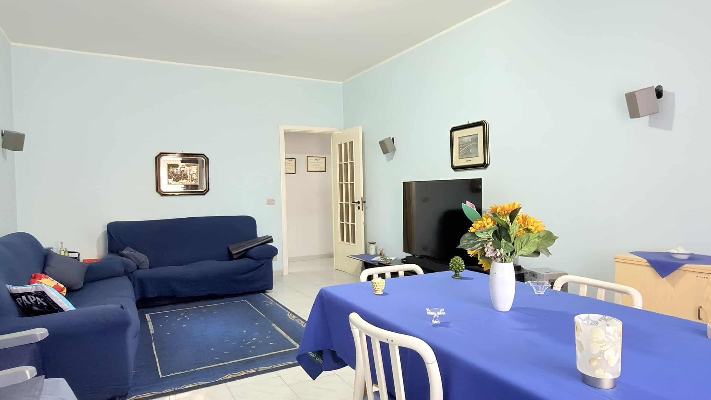 Elegante soggiorno con divani blu, tavolo con tovaglia blu, televisore e decorazioni moderne, ideale per vivere momenti di relax e convivialità in un ambiente accogliente e raffinato.