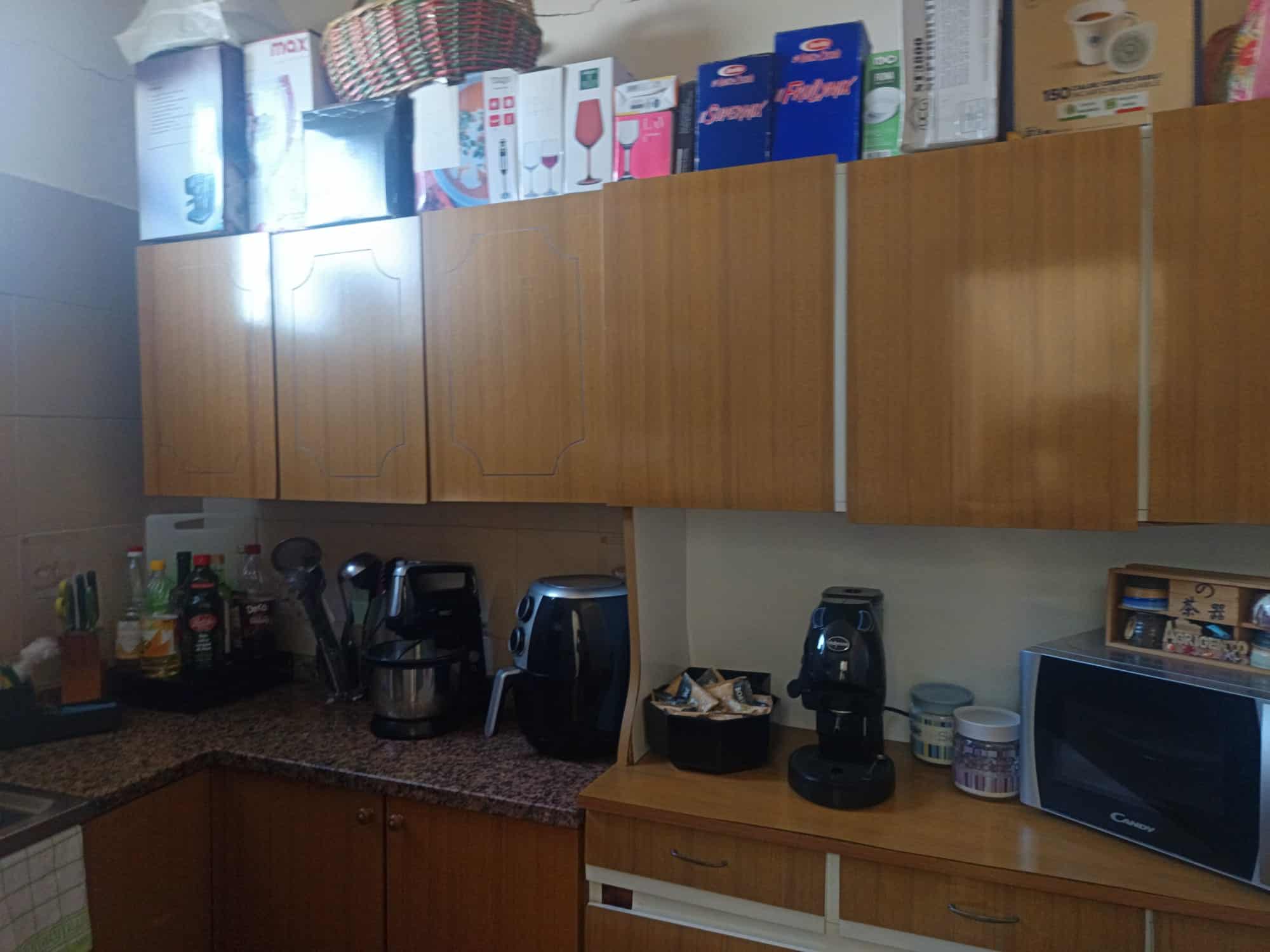 Una cucina moderna con armadietti in legno, elettrodomestici come macchina da caffè, microonde e frigorifero, e vari contenitori e utensili da cucina, ideale per spazi abitativi funzionali e accoglien.