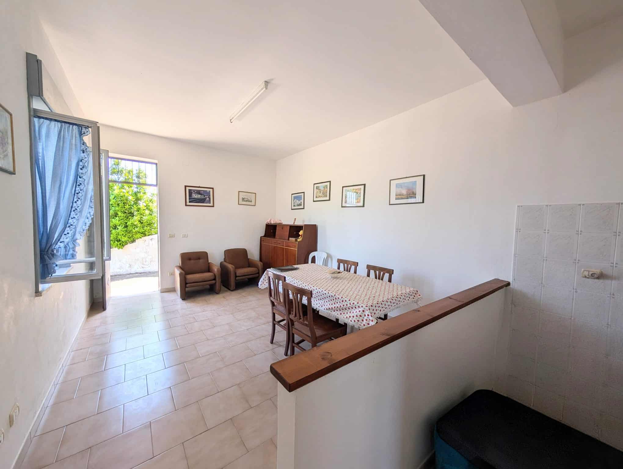 Ampia sala soggiorno con tavolo da pranzo, sedie e poltrone, pareti decorate con quadri, finestra aperta con tende blu, luce naturale, ambiente luminoso e accogliente, ideale per vivere momenti di rel.