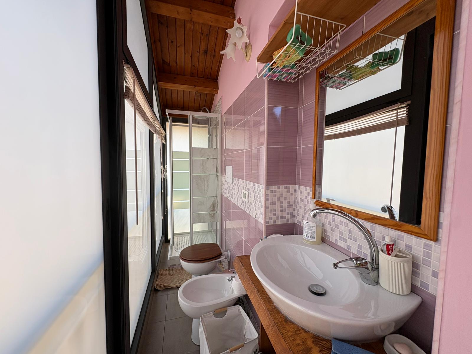 Lavabo da bagno con finestra, pareti rosa e accessori di arredo, in un ambiente luminoso e accogliente, ideale per spazi di relax e cura personale.