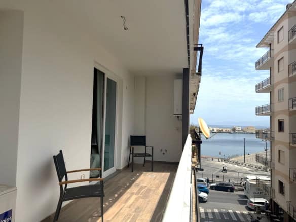 Balcone di un appartamento con vista sul mare, arredato con sedie in legno e spazio per relax, in un complesso residenziale vicino alla costa.