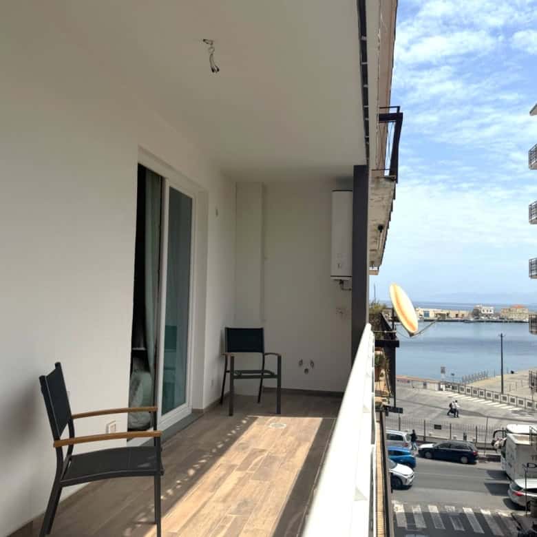 Balcone di un appartamento con vista sul mare, arredato con sedie in legno e spazio per relax, in un complesso residenziale vicino alla costa.