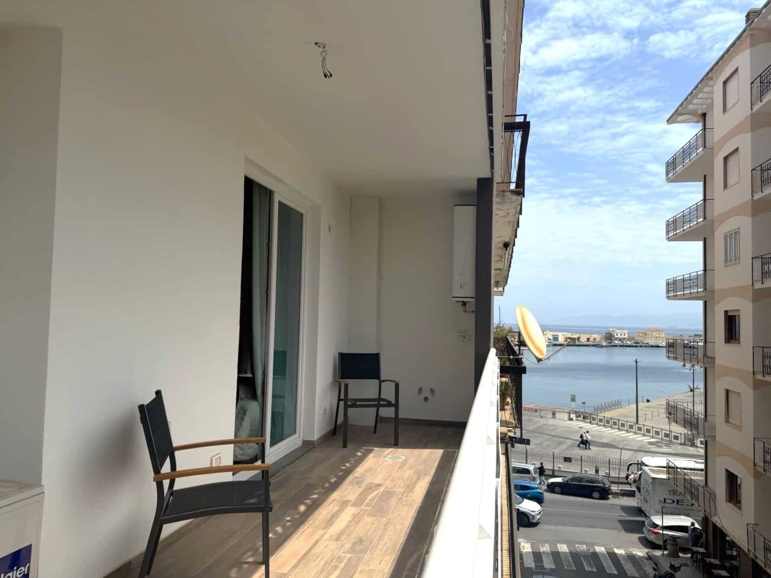 Balcone di un appartamento con vista sul mare, arredato con sedie in legno e spazio per relax, in un complesso residenziale vicino alla costa.