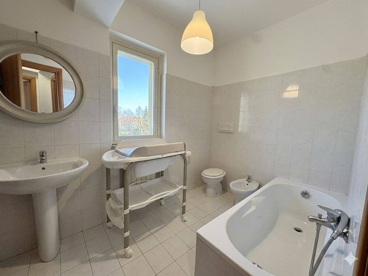 Lavabo, bidet e vasca da bagno in un bagno luminoso con finestra, arredato in stile semplice e funzionale, ideale per ambienti di casa moderni e pratici.