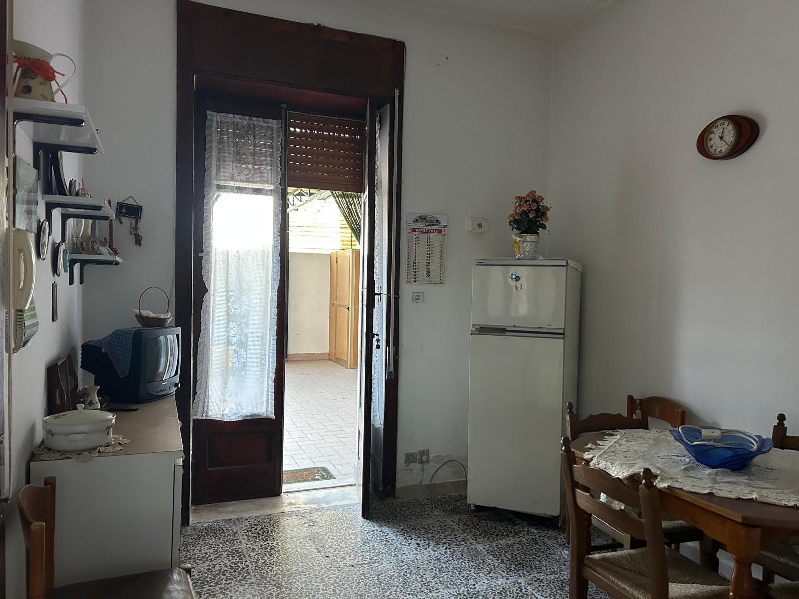 Interno di una cucina con porta finestra che apre su un balcone, arredamento semplice e funzionale, elettrodomestici e mobili in stile classico.