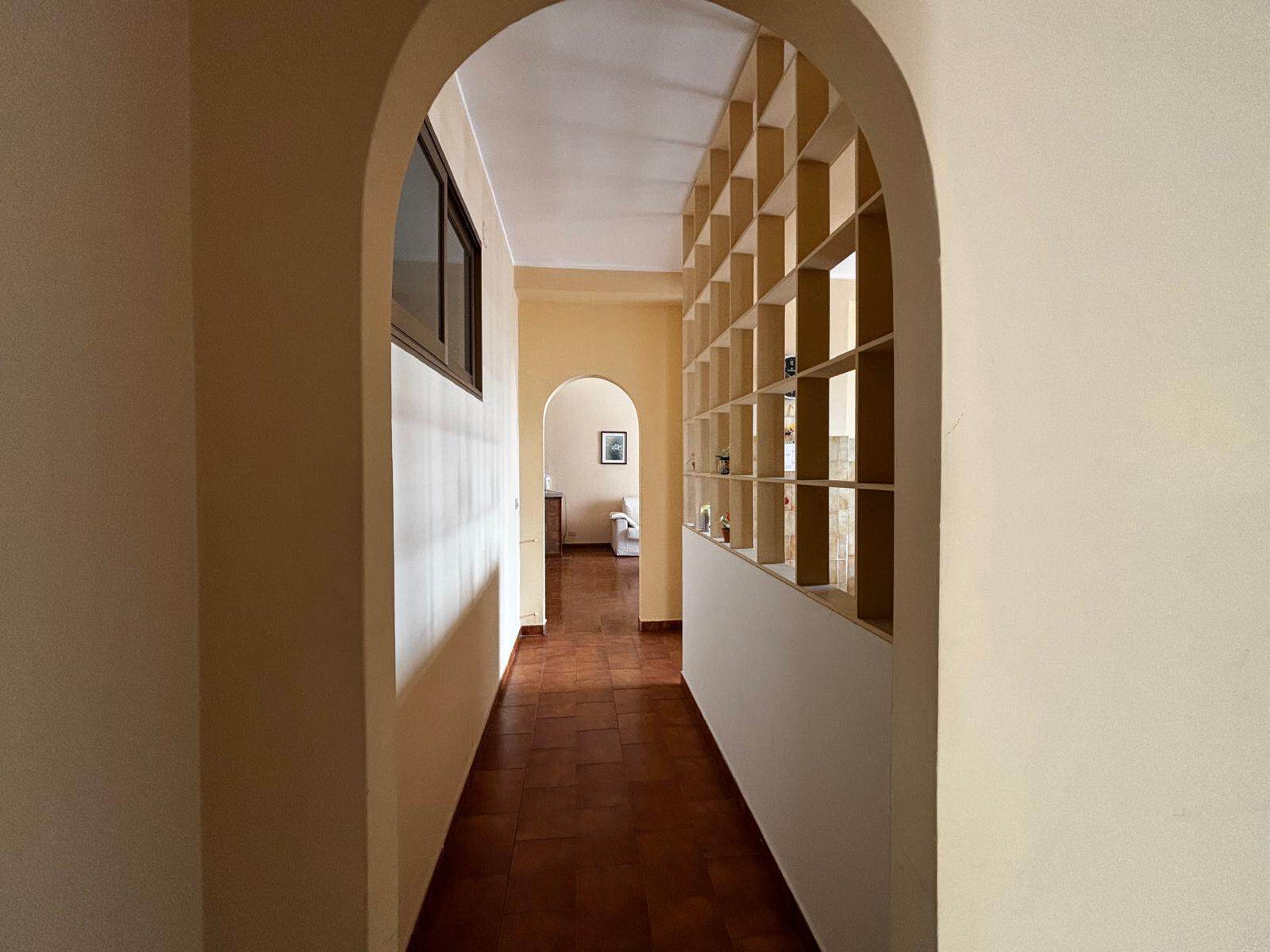 Elegante corridoio interno con archi e scaffalature in legno, luminoso e accogliente, ideale per ambienti residenziali moderni e funzionali. Perfetto esempio di design abitativo in stile contemporaneo.