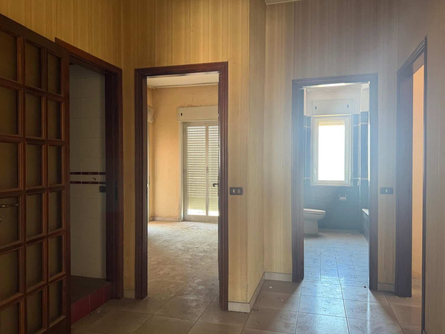 Interno di un appartamento con pareti in legno, porte in legno e finestre luminose, ideale per ristrutturazione o investimento immobiliare.