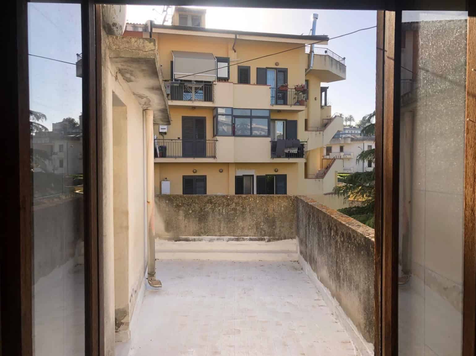 Balcone di un appartamento con vista su edificio residenziale moderno, pareti in cemento e ringhiera in metallo, luce naturale, ambiente urbano, spazio esterno privato, ideale per relax e svago.