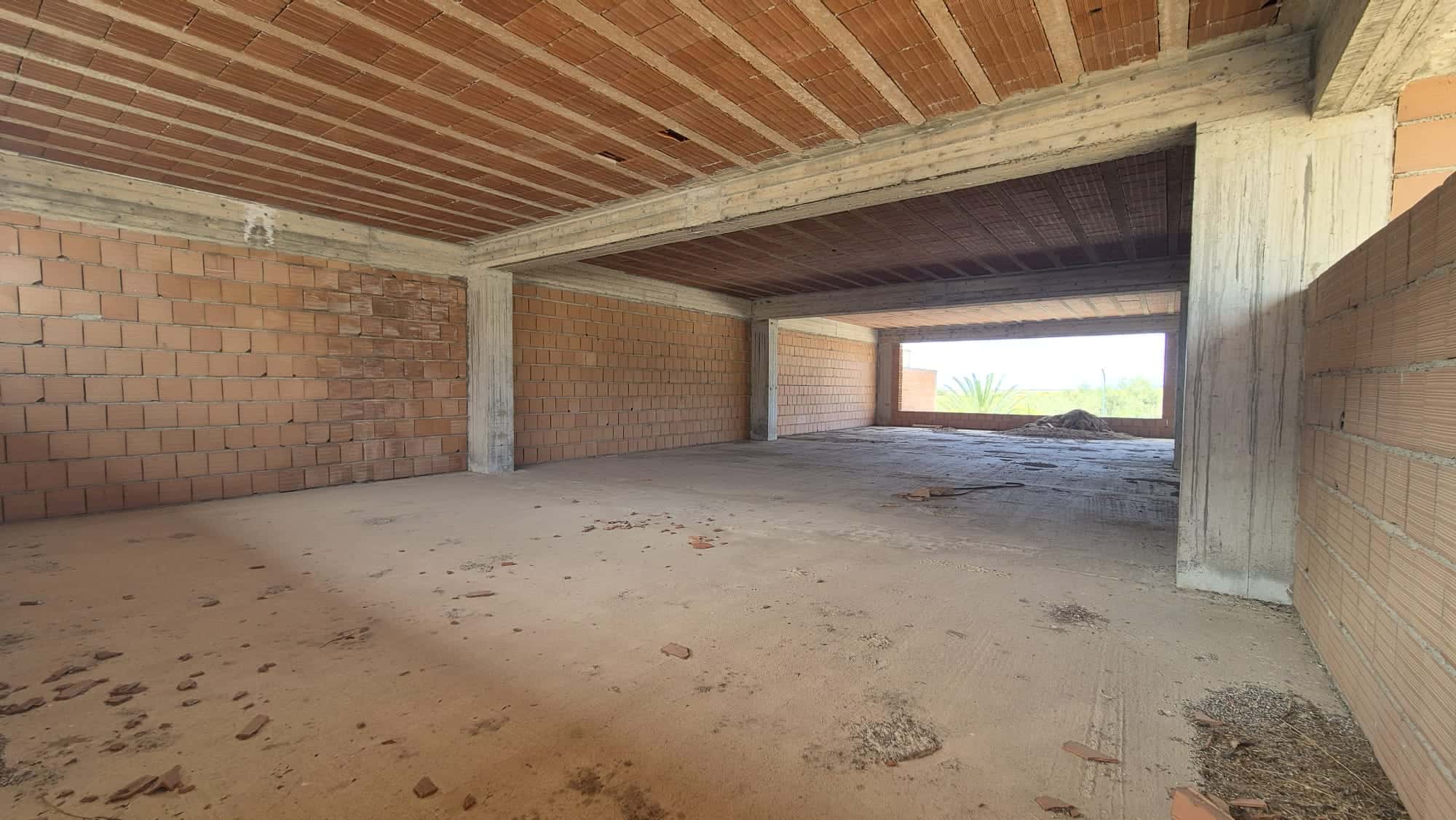 Ampio spazio interno di un edificio in costruzione con pareti in mattoni e soffitto in legno, pronto per essere rifinito e personalizzato.