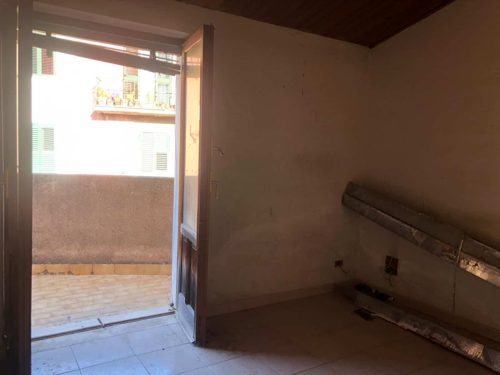 Interno di un appartamento vuoto con porta aperta che dà su un balcone, pareti neutre e pavimento in piastrelle, pronto per ristrutturazione o arredamento.
