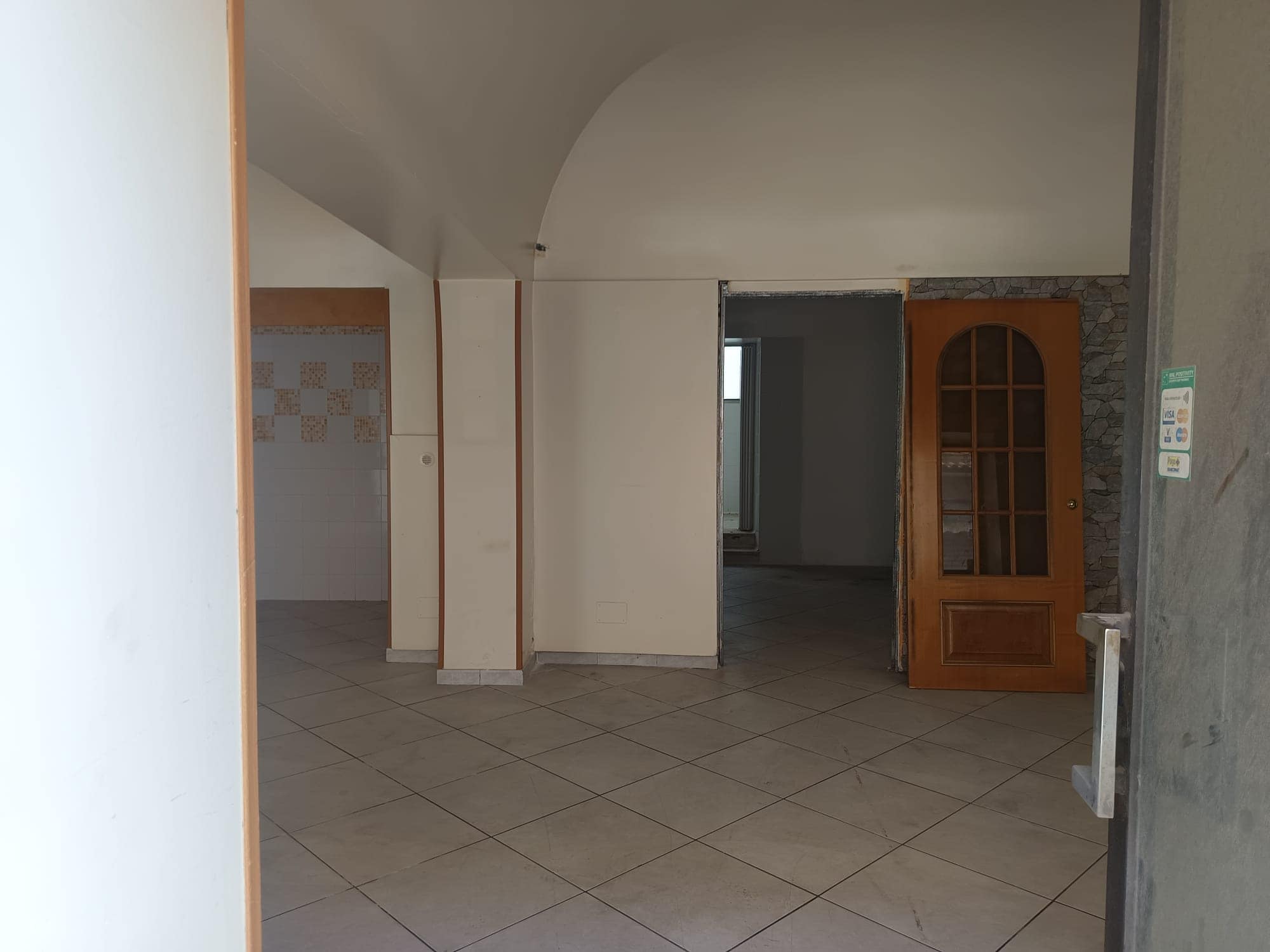 Spazio interno di un appartamento in fase di ristrutturazione con pareti bianche, pavimento in piastrelle e porta in legno con vetrata, pronto per essere arredato.