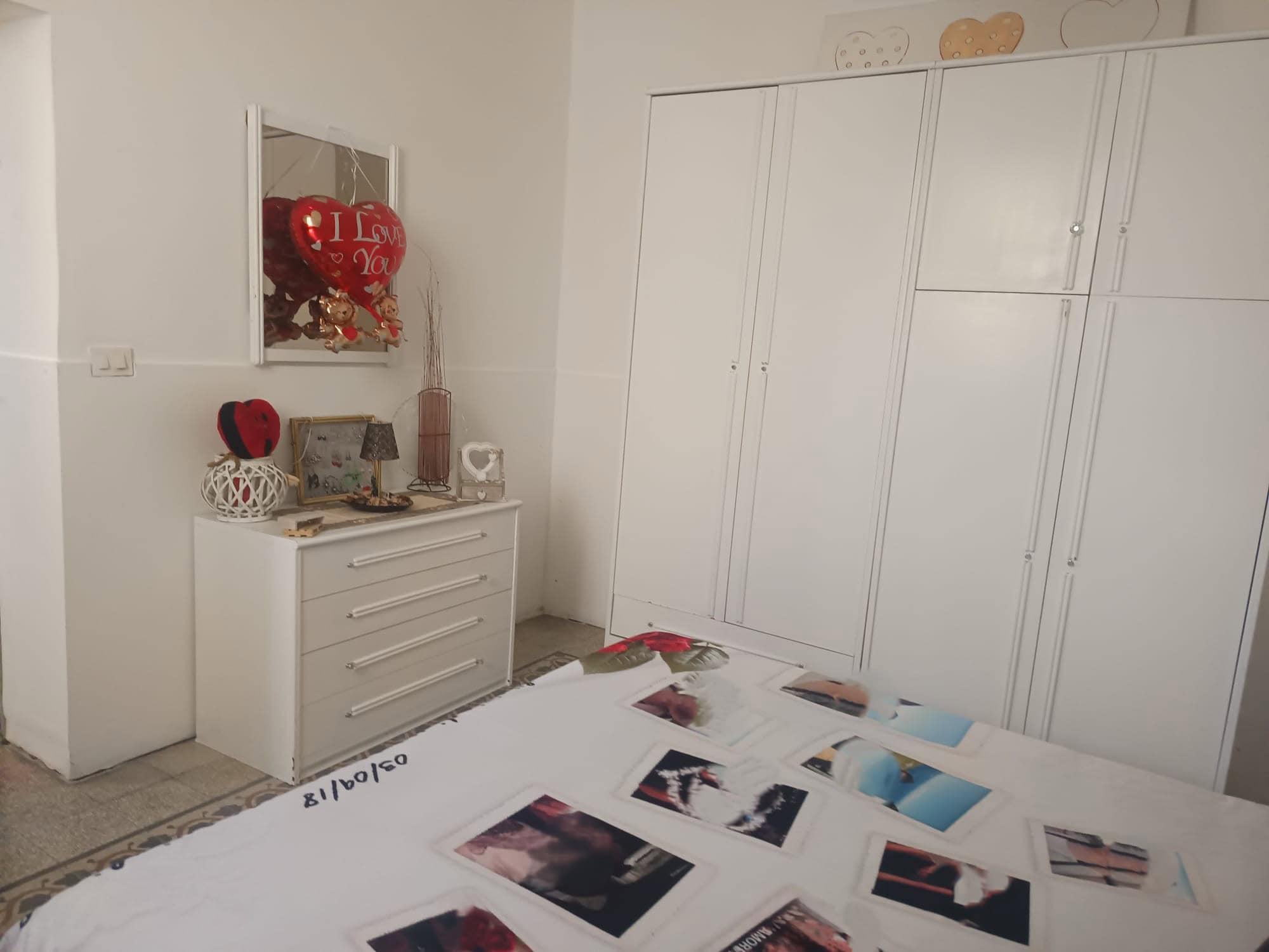 Armadio a muro bianco con ante scorrevoli in una camera da letto moderna, decorata con oggetti romantici e fotografie personali.