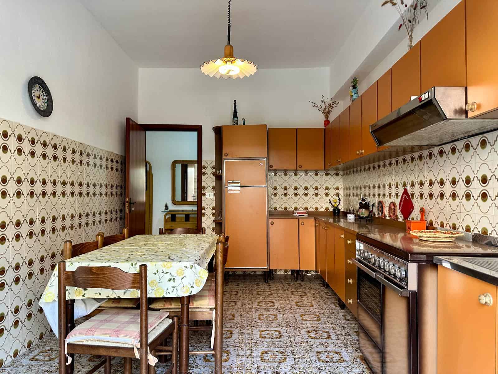 Cucina abitabile con mobili arancioni, piano cottura a gas e pareti rivestite con piastrelle decorative vintage, ambiente luminoso e accogliente.
