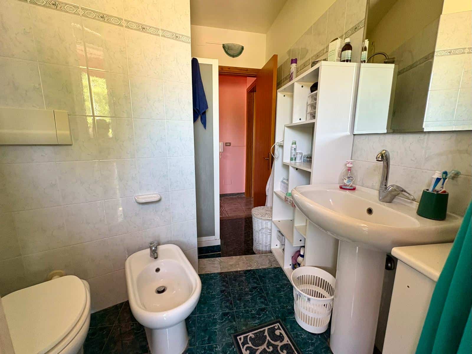 Lavandino e bidet in bagno con piastrelle chiare, specchio e accessori per l'igiene, ambiente funzionale e ben illuminato, ideale per servizi igienici domestici o di appartamenti in vendita o affitto.