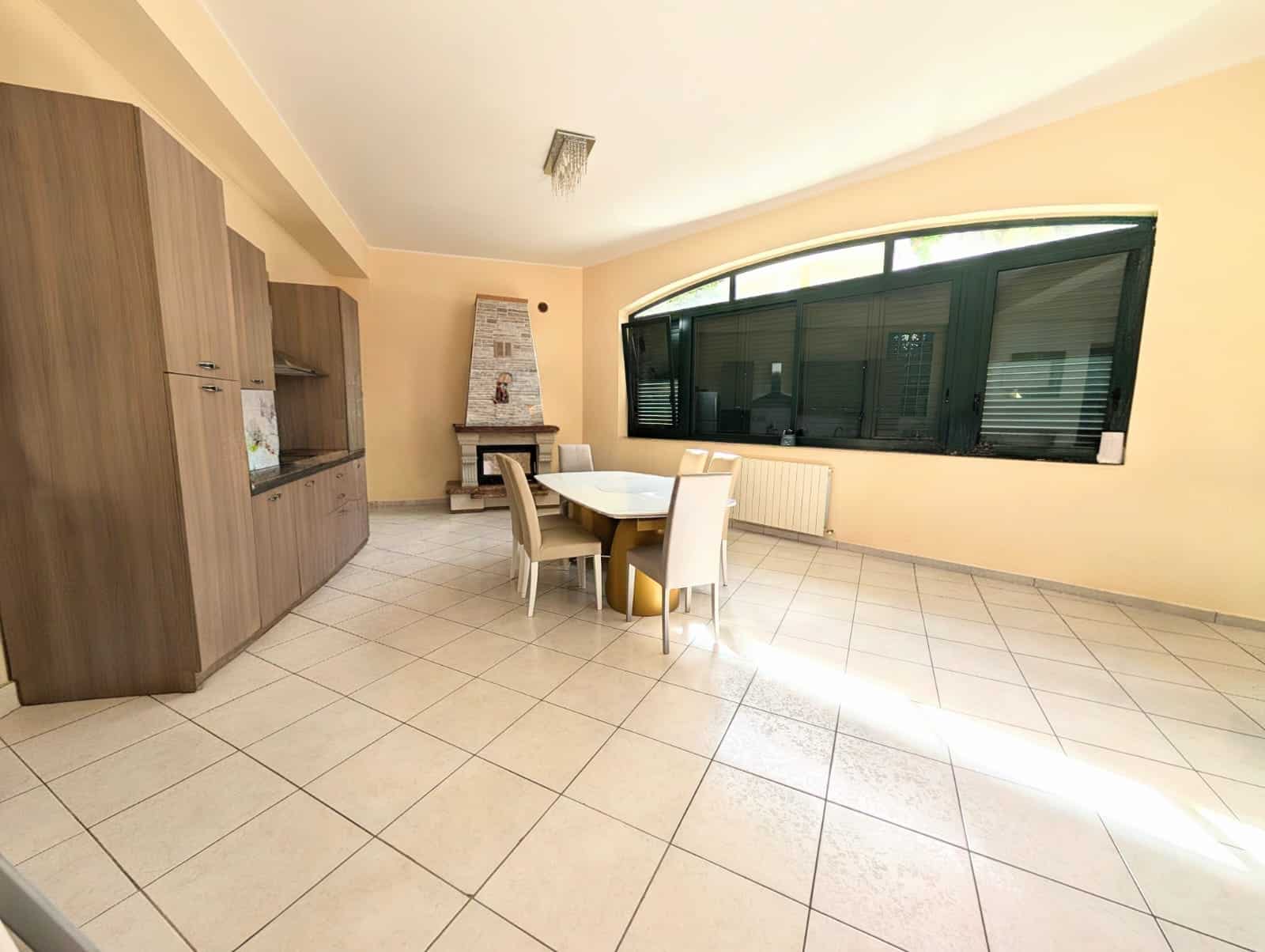 Sala da pranzo luminosa con grande finestra curva, mobili in legno e camino, ideale per ambienti residenziali moderni e accoglienti.